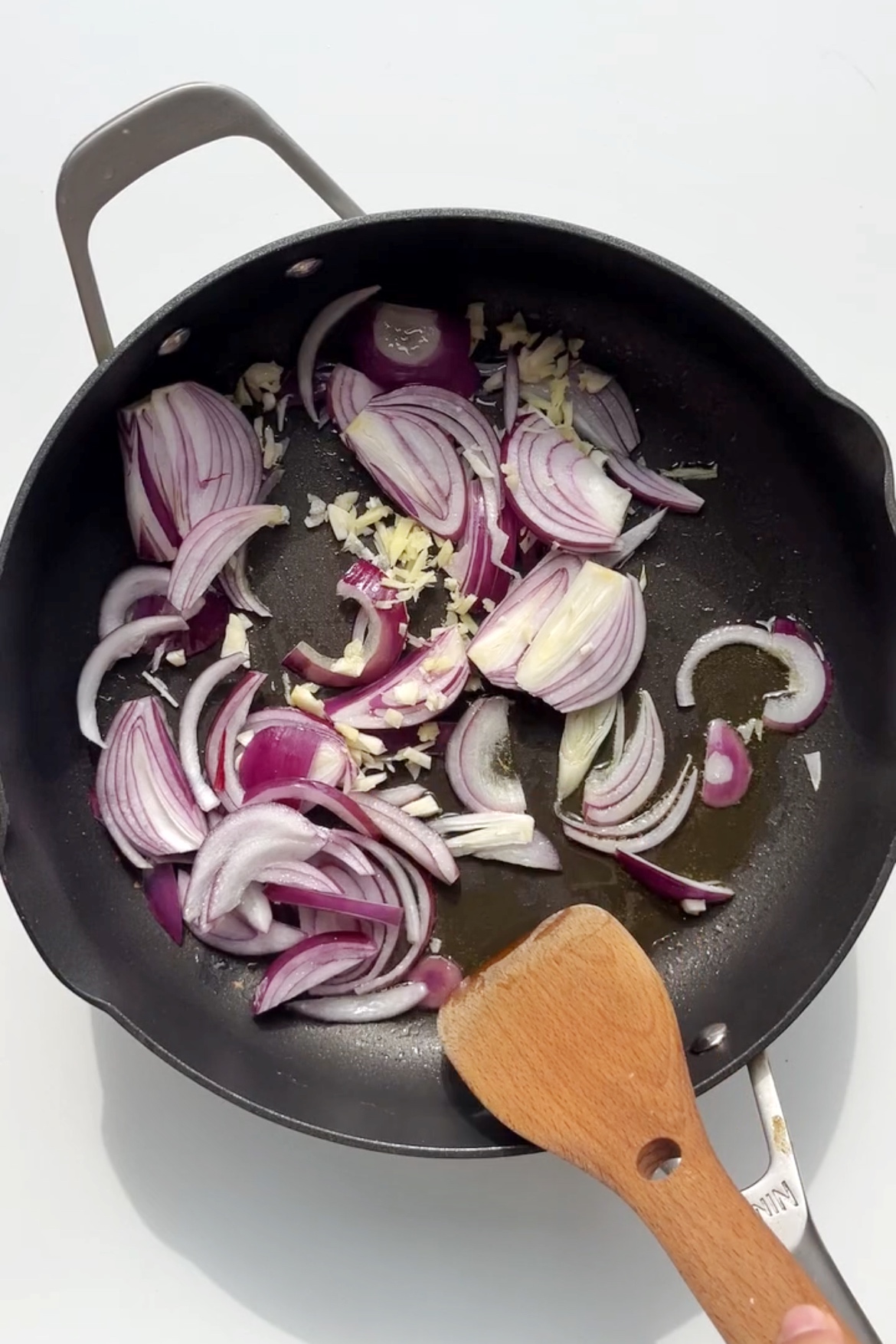 Red onion, garlic, and ginger frying in a black non-stick frying pan.