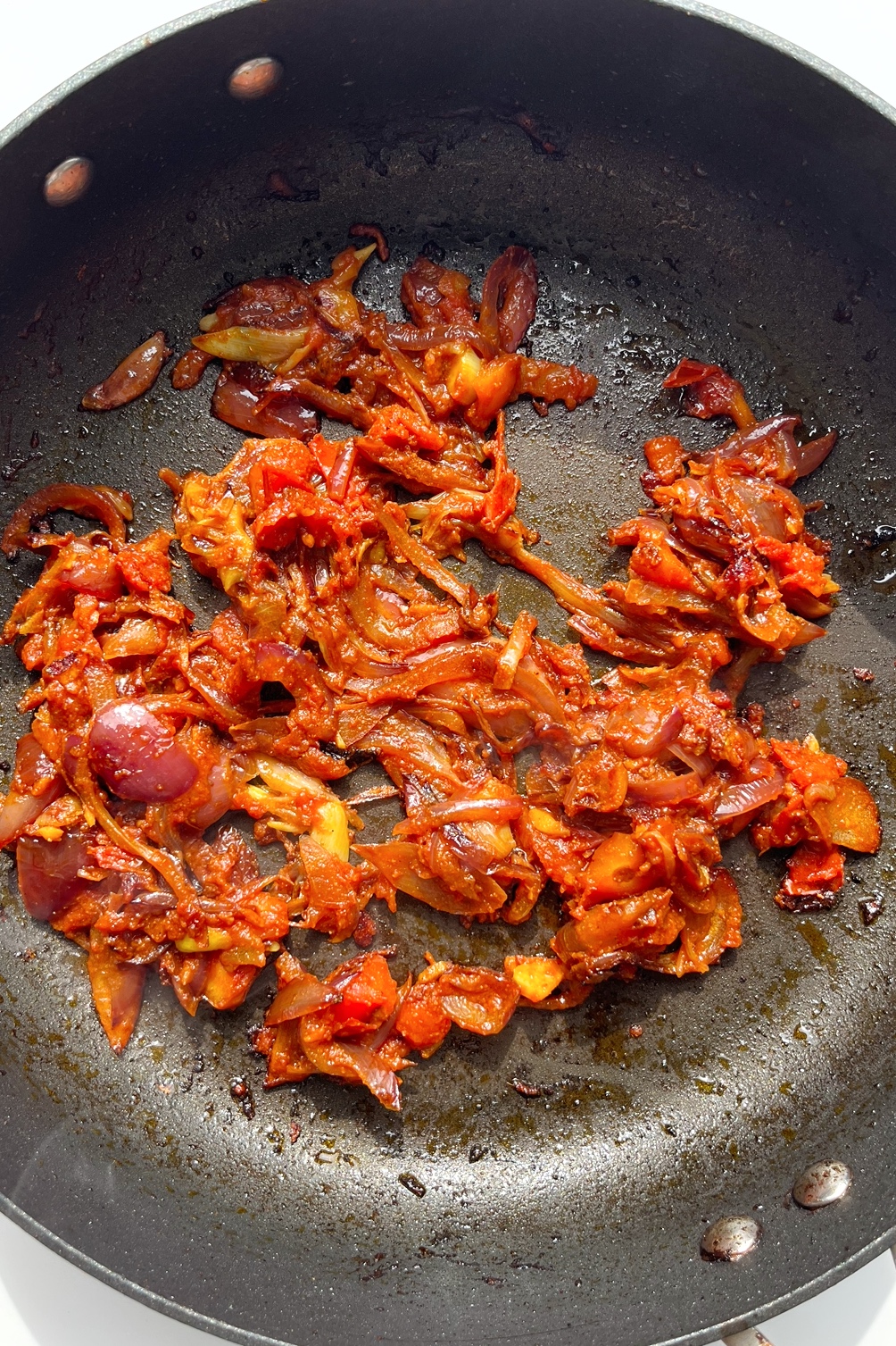 Red onion, garlic, and ginger, with tomatoes and spices in a non-stick frying pan.