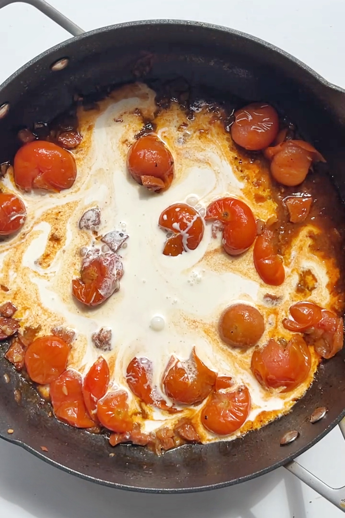 Making tomato and single cream sauce in black frying pan.