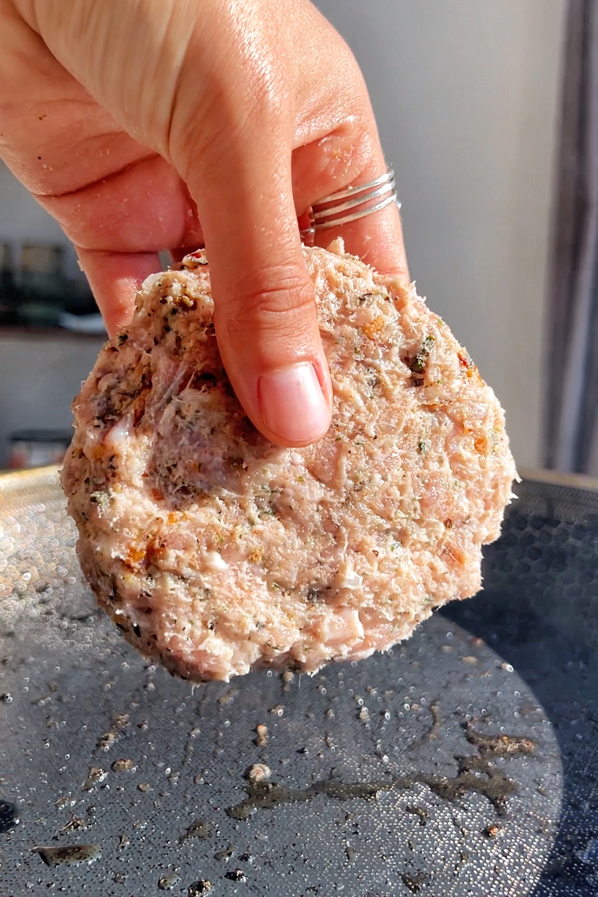 Sausage patty that is raw and being placed into a pan.