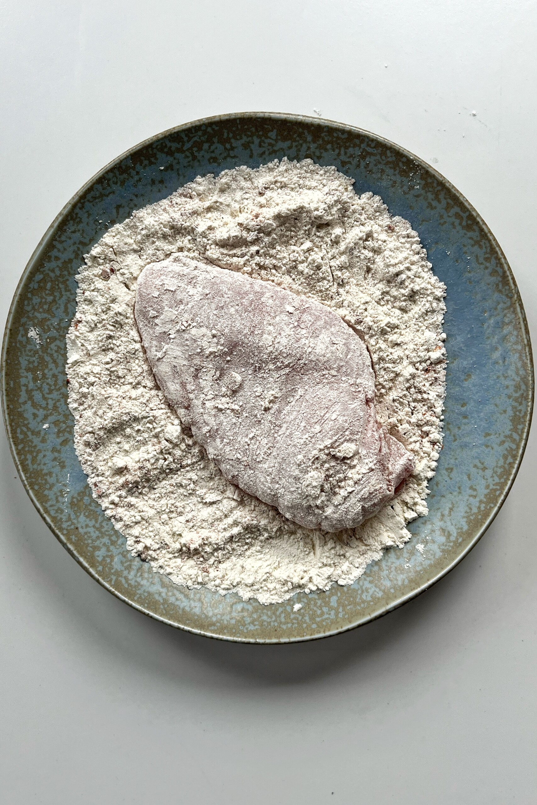 Dredging chicken breast in a flour mixture. 