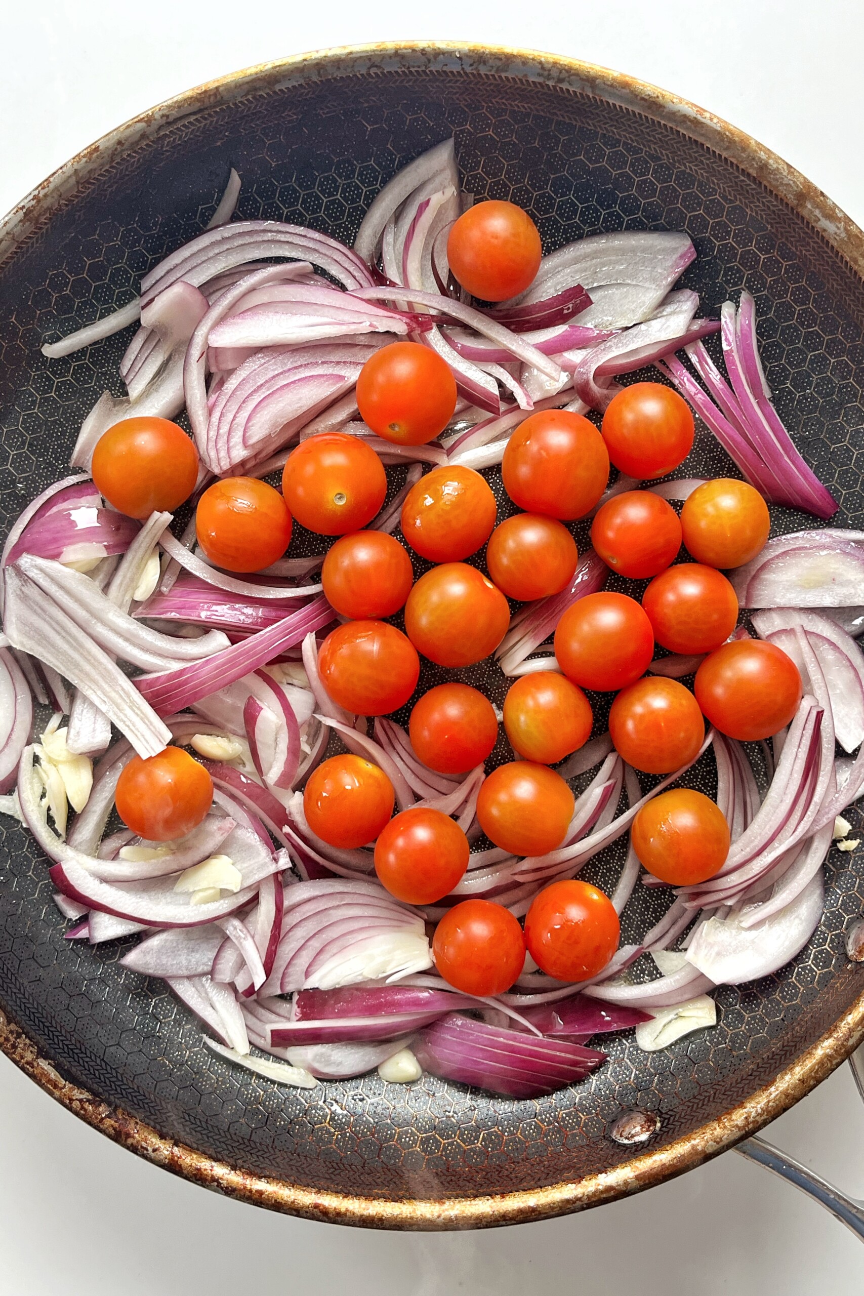 Tomatoes, red onion, and garlic frying in a pan.