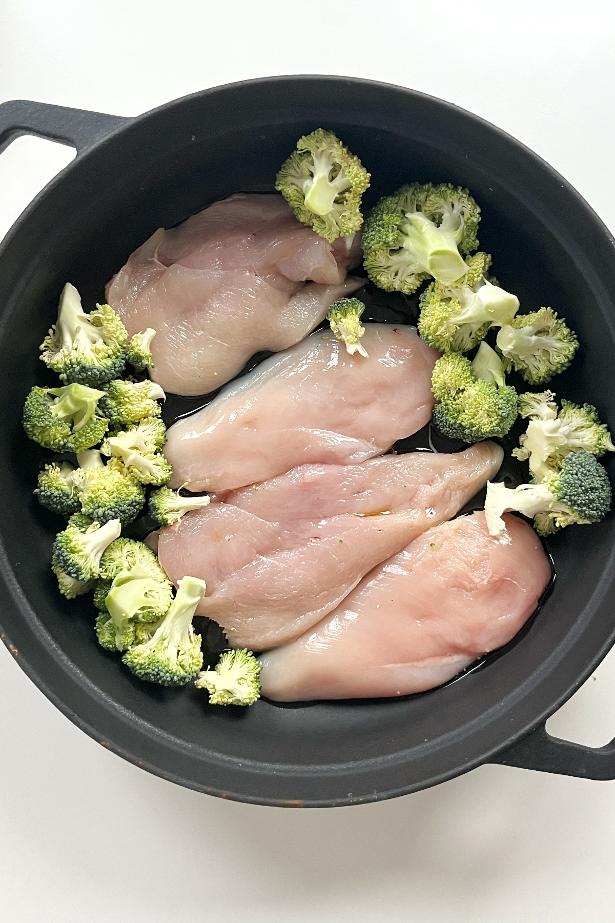 Black pan with 4 pieces of chicken inside and broccoli florets.