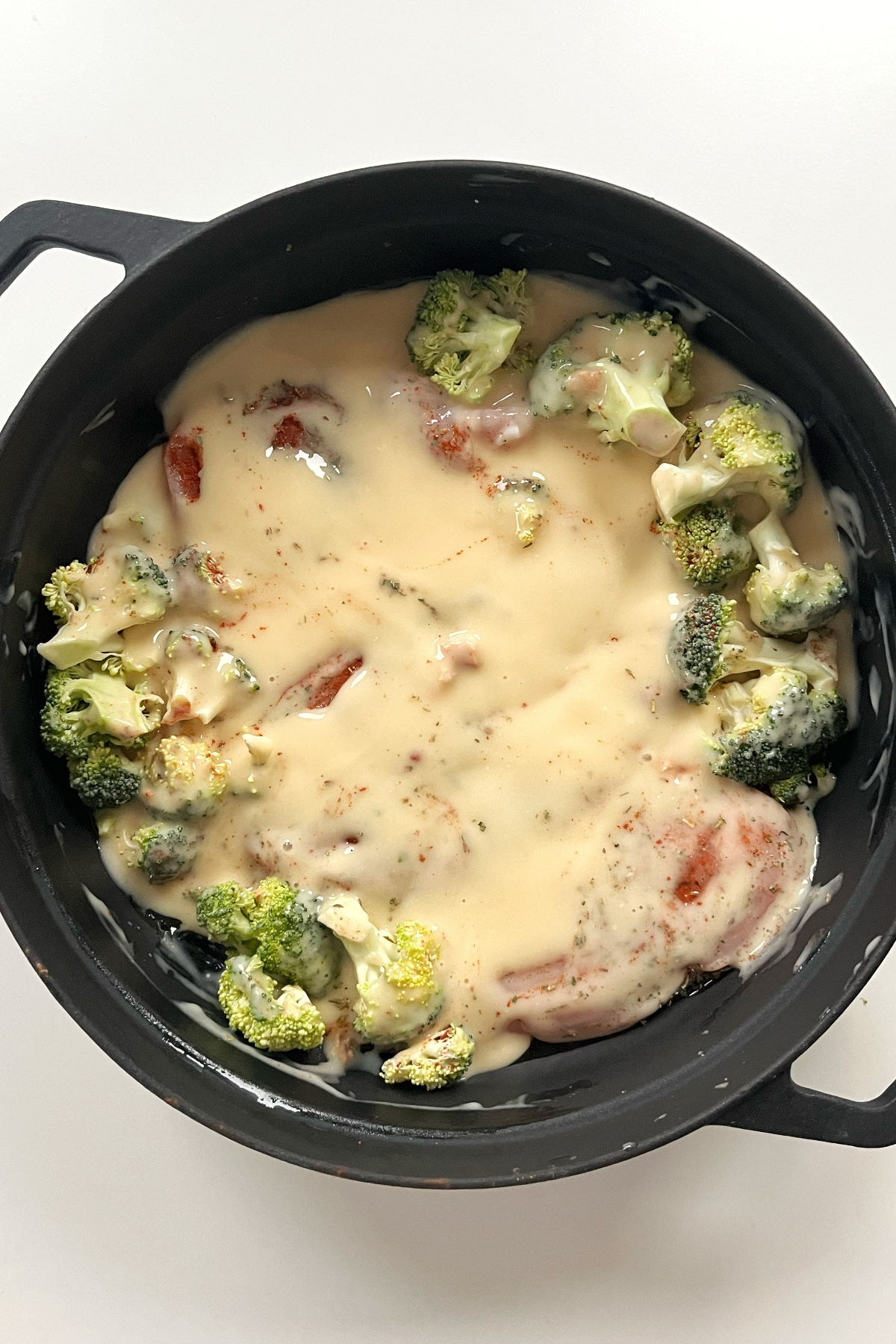 Black pan filled with chicken breast, broccoli, cream of chicken soup.