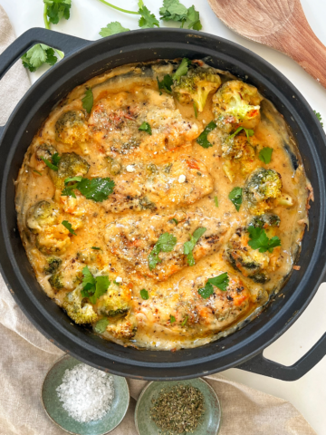 Cheesy baked chicken in a black pan topped with parsley.