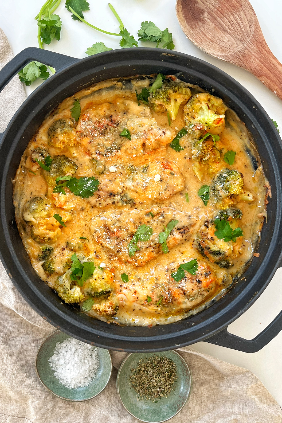 Cheesy baked chicken in a black pan topped with parsley. 