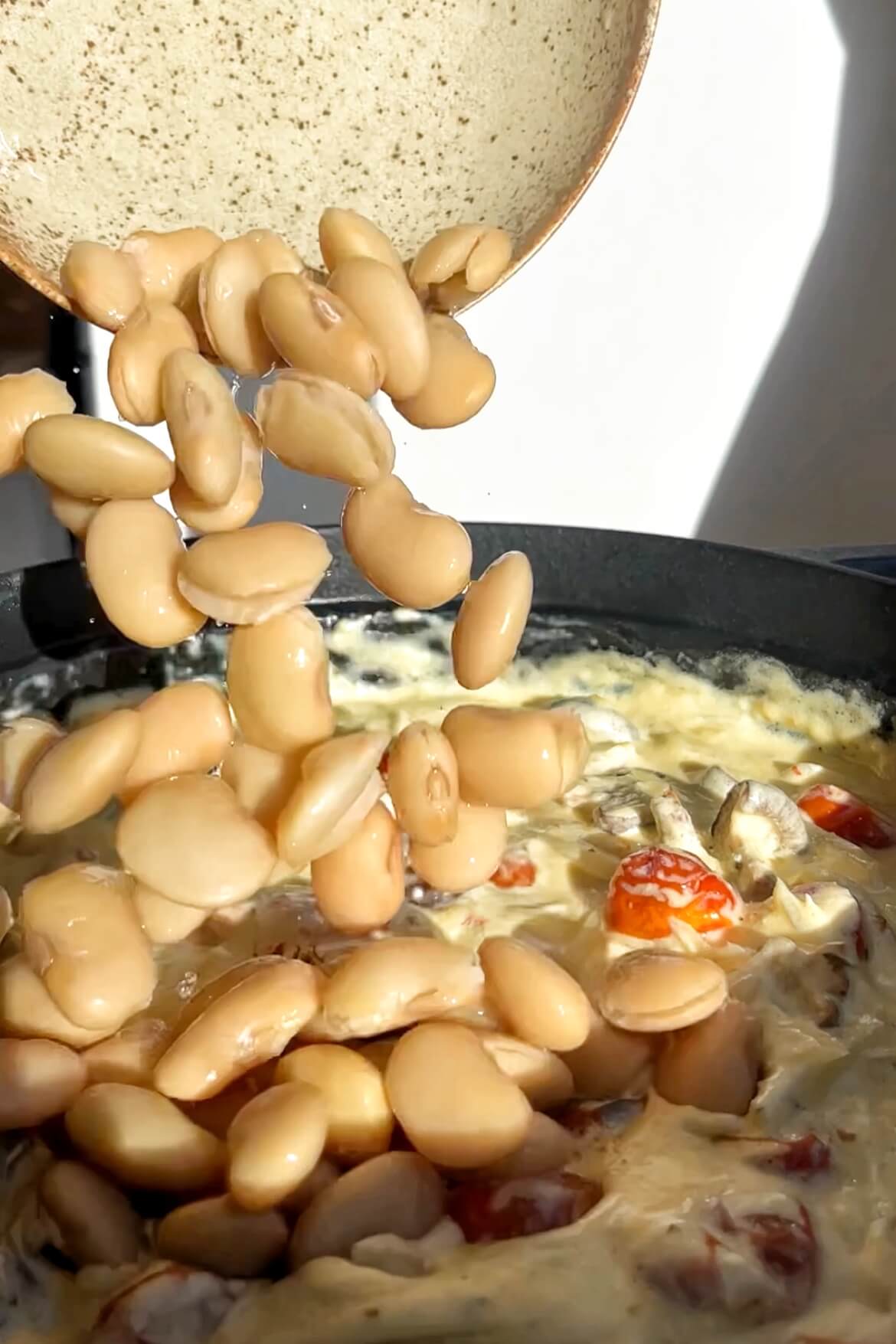 Pouring butter beans into a pan. 