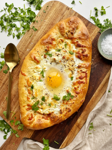 Cheese boat pie with egg in the middle on a brown wooden board.