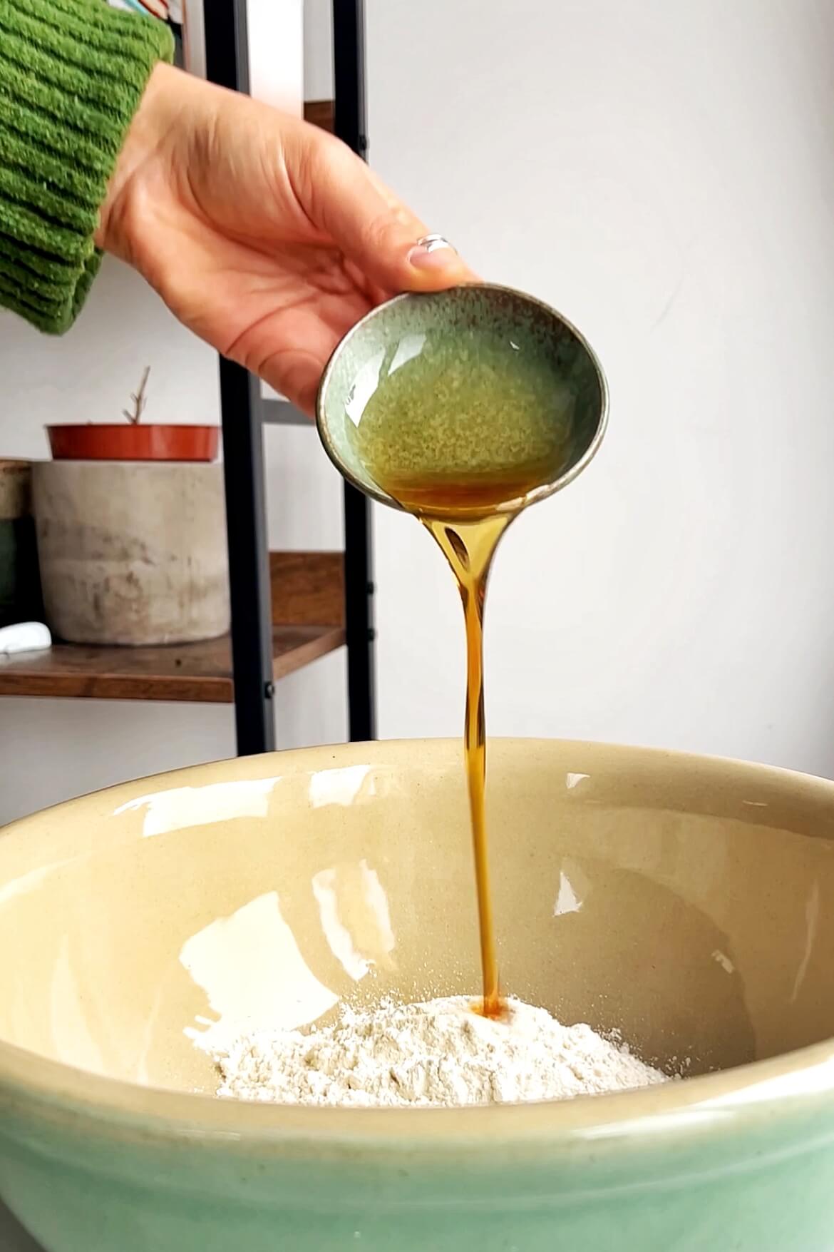Pouring sesame oil into bowl of flour. 