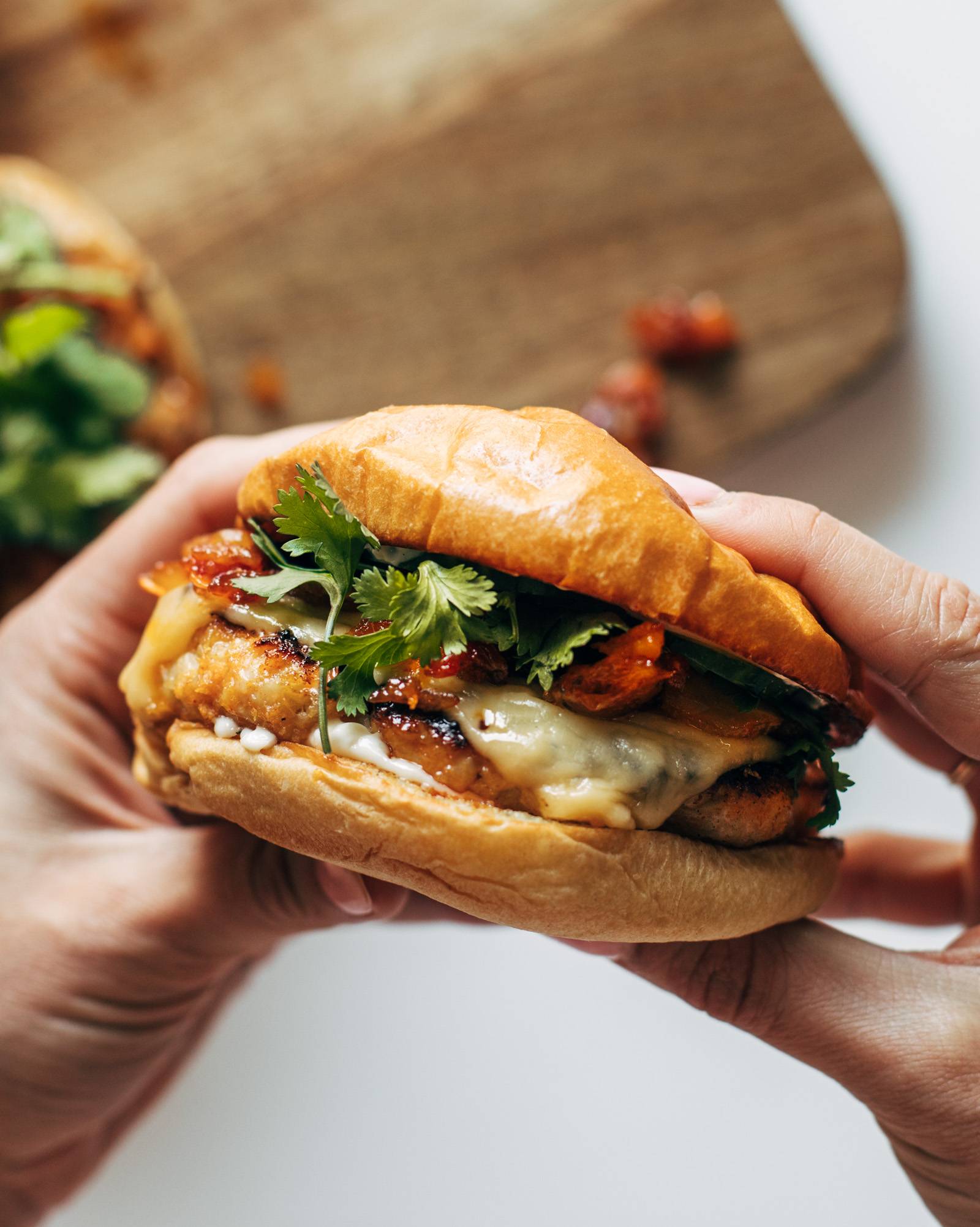 Gochujang burgers with chicken and kimchi held by two hands.