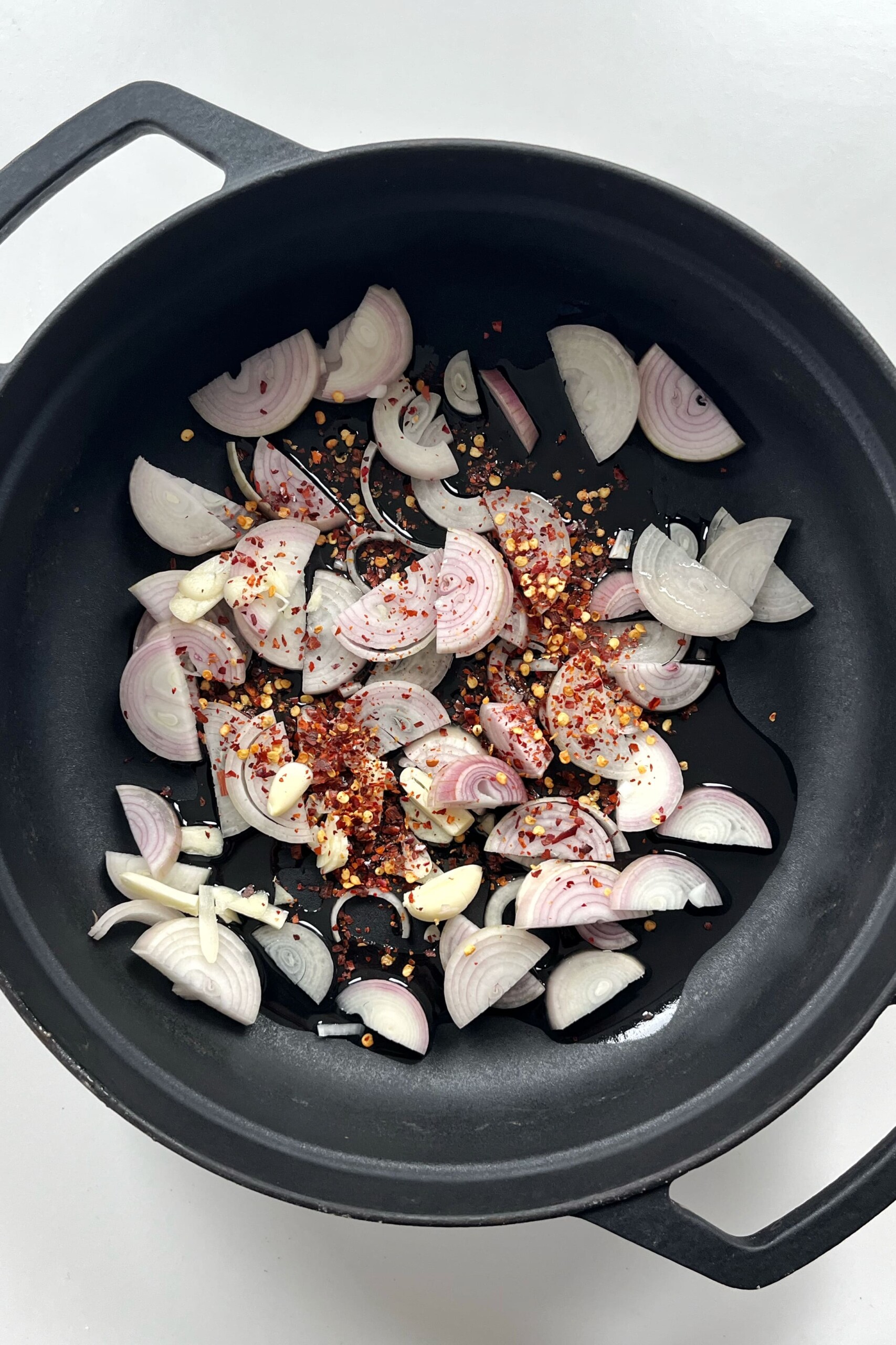 Frying shallots, garlic, chilli flakes in a black pan.