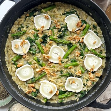 Asparagus orzotto topped with walnuts and goats cheese in a black pan.