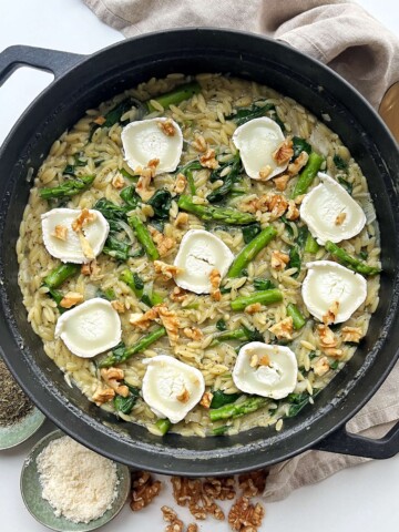 Asparagus orzotto topped with walnuts and goats cheese in a black pan.