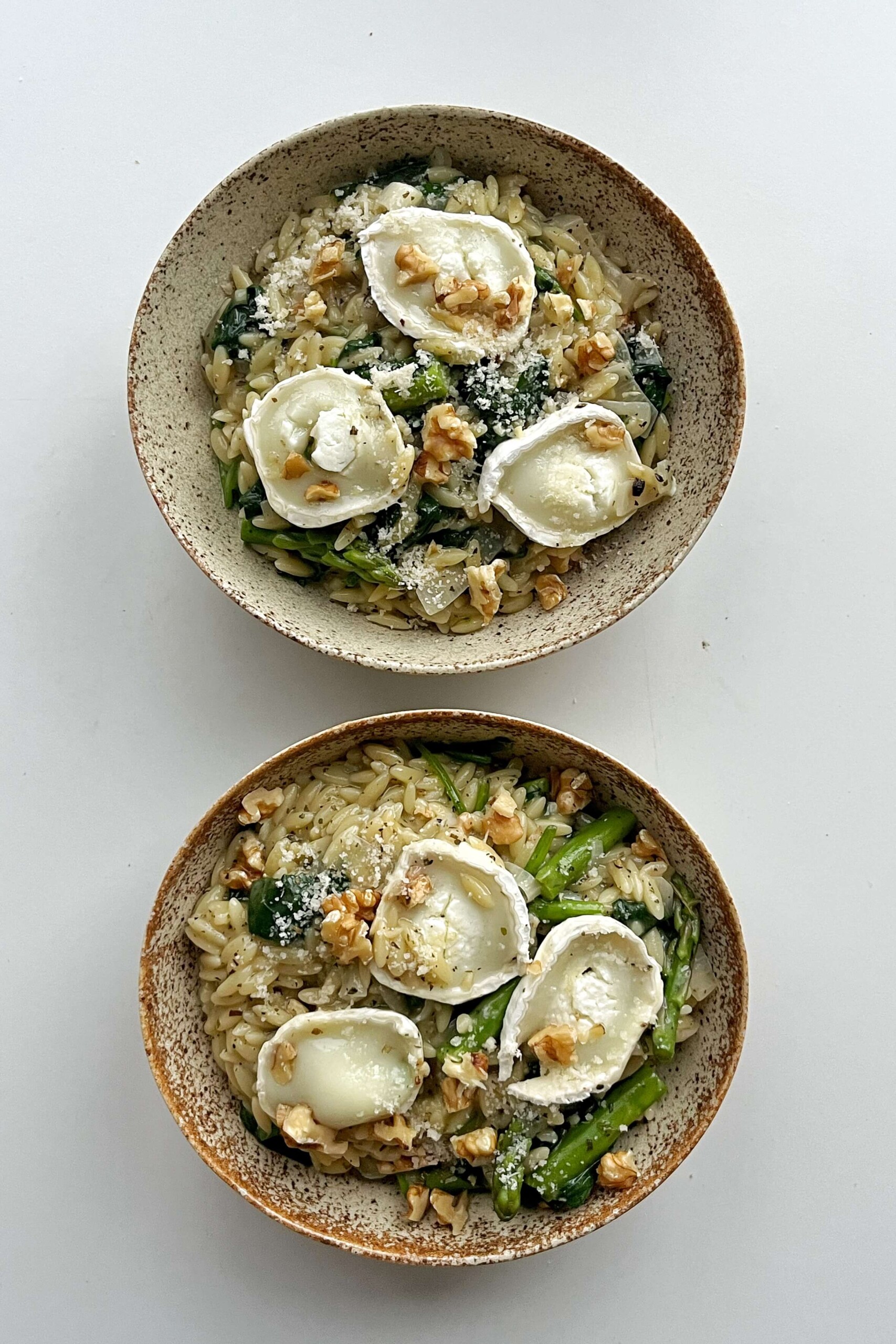 Two bowls of asparagus orzotto topped with goats cheese. 