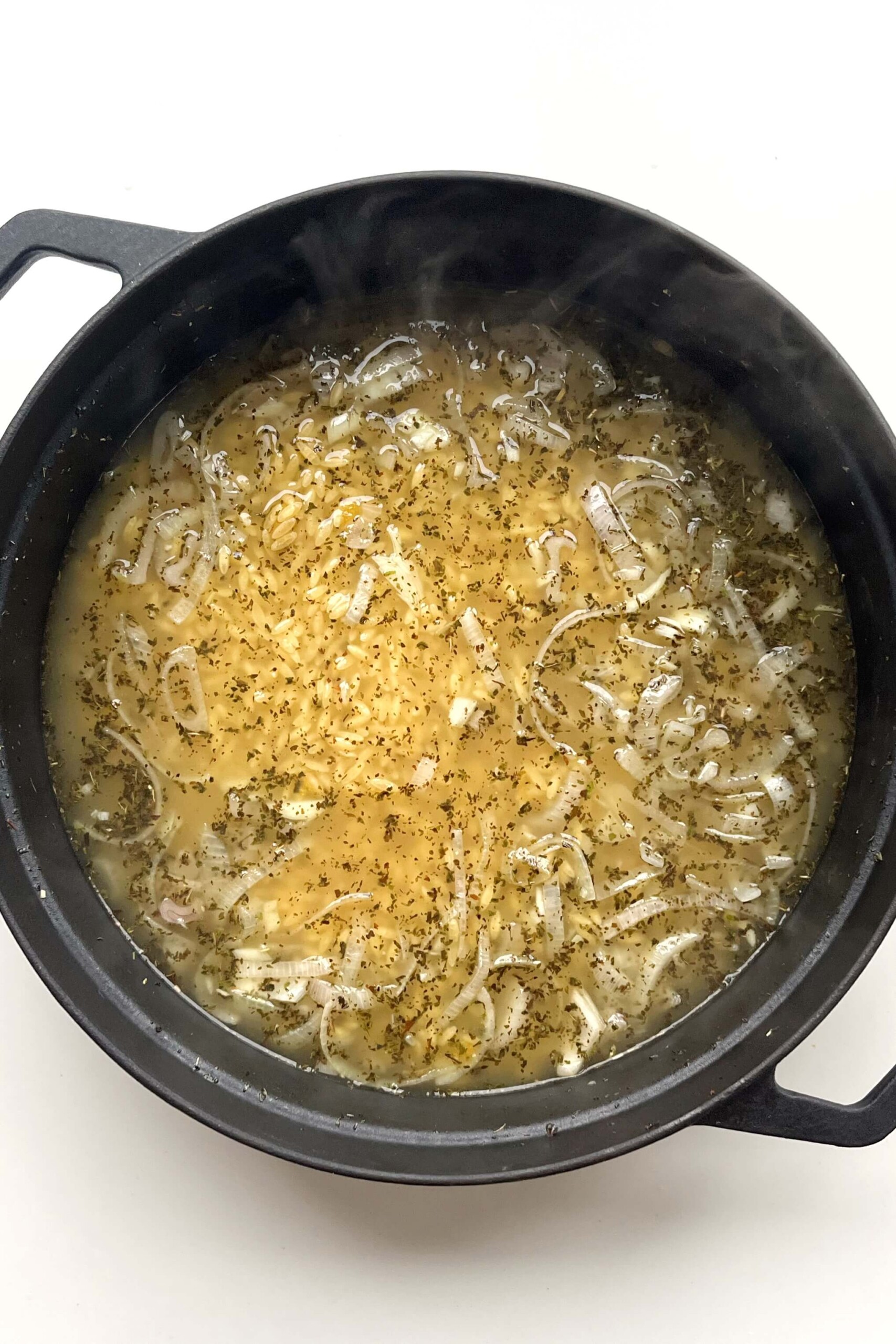 Black pan with orzo and stock inside. 