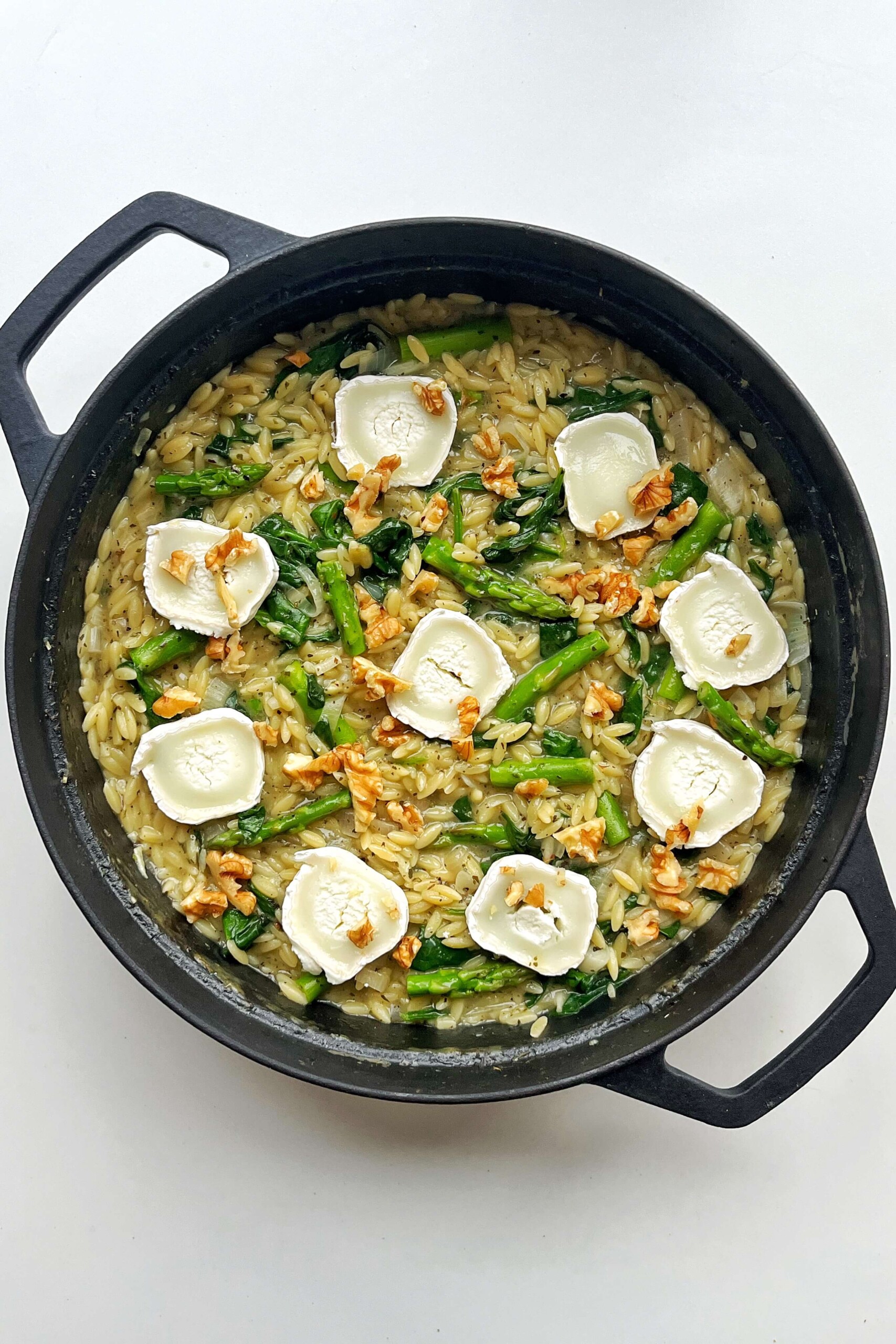 Orzotto with asparagus topped with goats cheese in a black pan.