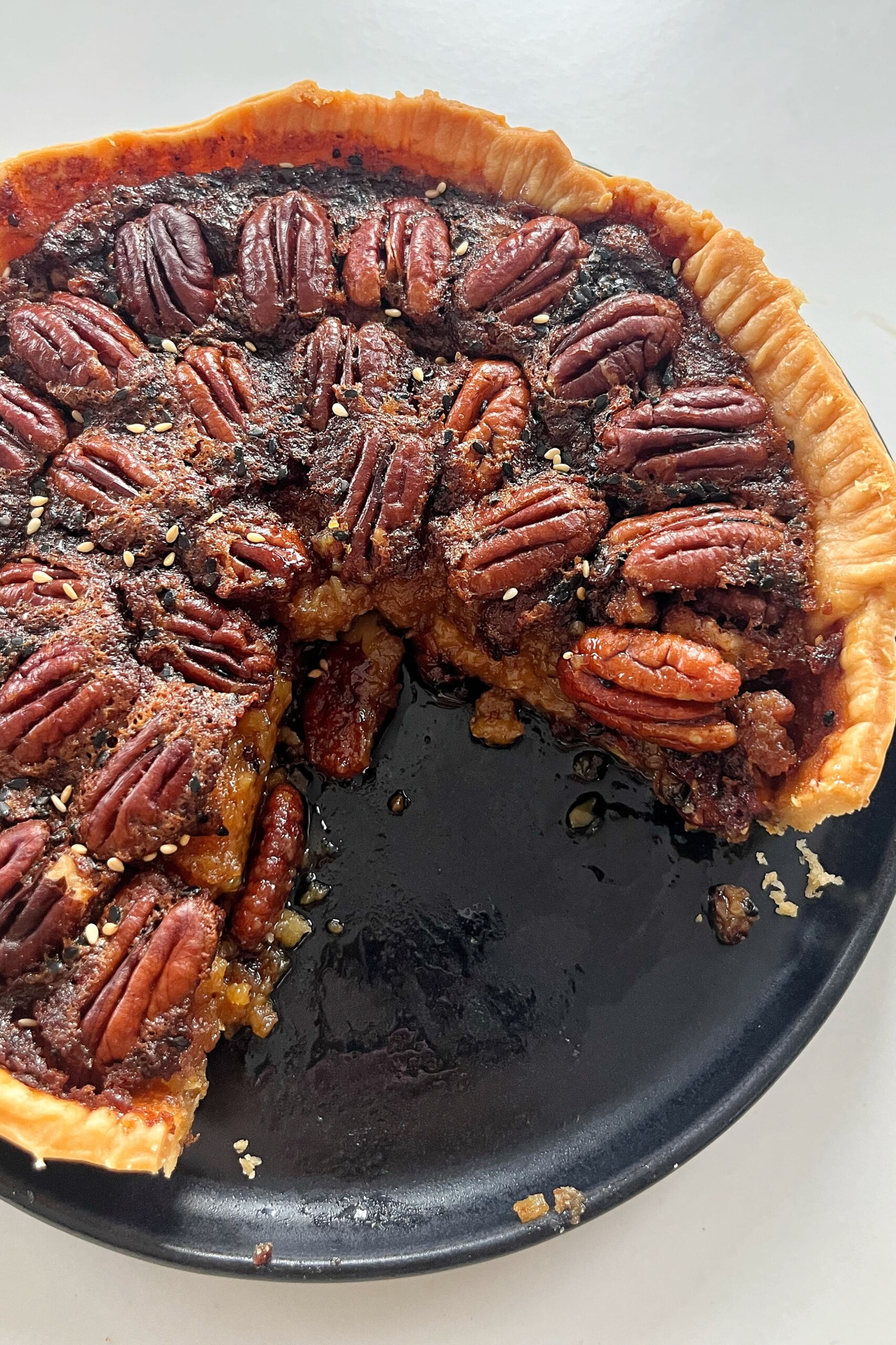Miso pecan pie that has a slice cut out of it on a black plate.