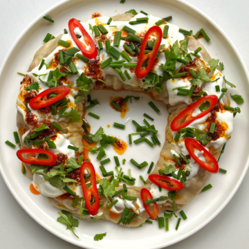 Dumpling wreath on a white plate topped with yoghurt, harissa oil, chives, and sliced chilli.