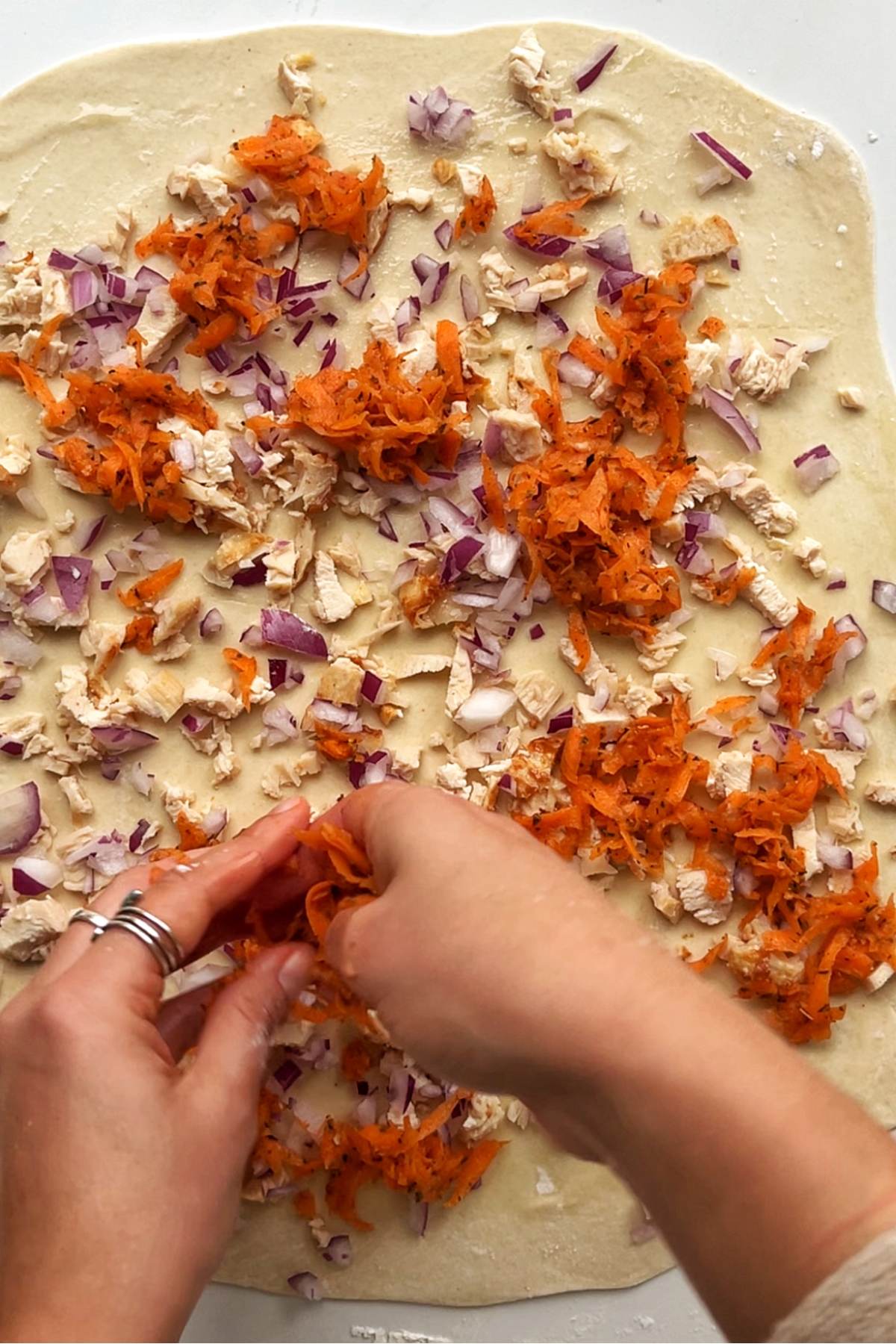 Placing leftover turkey, red onion, and grated carrot onto a large sheet of rolled out dough.