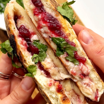 Opening of a festive turkey flatbread with cranberry sauce, brie, and turkey.