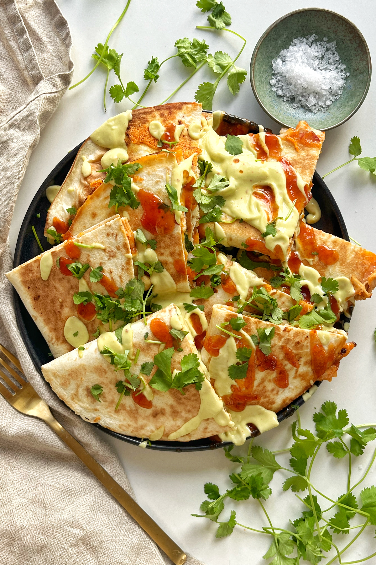 Top down image of turkey quesadillas on a black plate topped with avocado dressing and sweet chilli sauce.