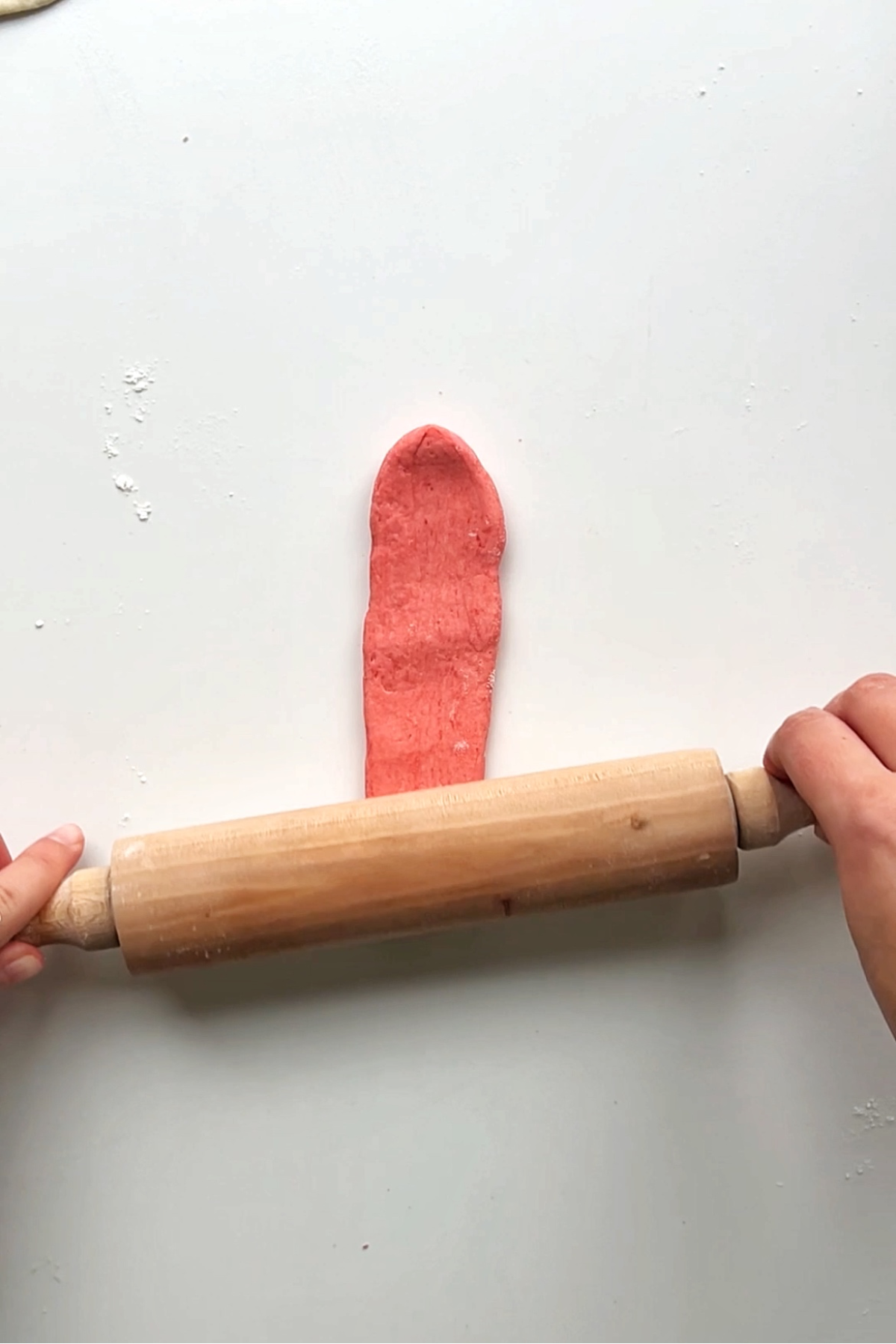 Rolling out pink piece of dough using rolling pin. 