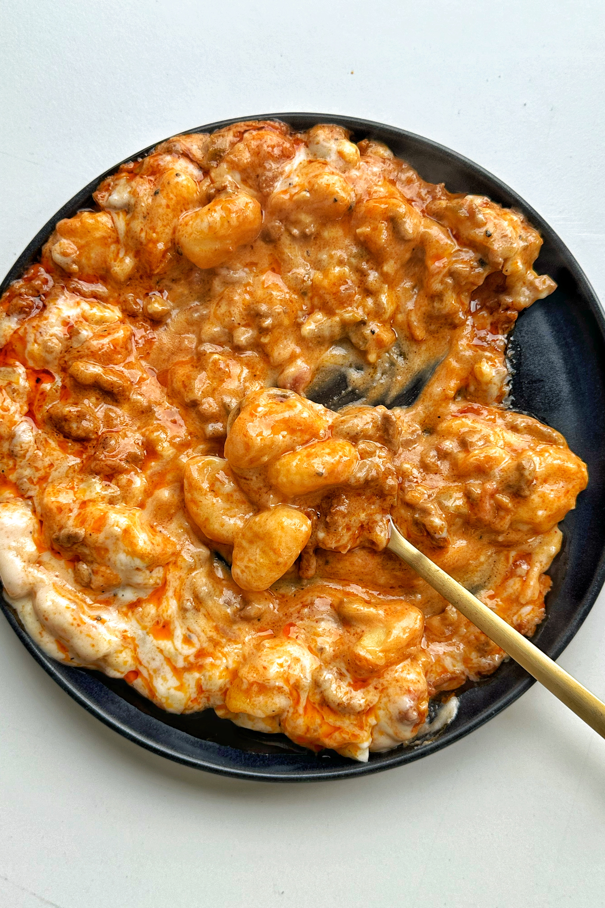 Plate of gochujang gnocchi lasagne on white background with golden spoon.