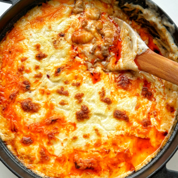 Black casserole dish filled with gochujang gnocchi lasagne with wooden spoon.