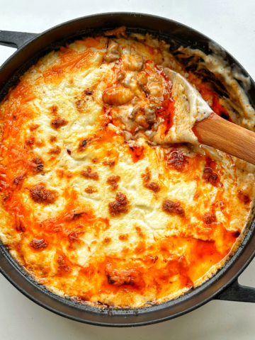 Black casserole dish filled with gochujang gnocchi lasagne with wooden spoon.