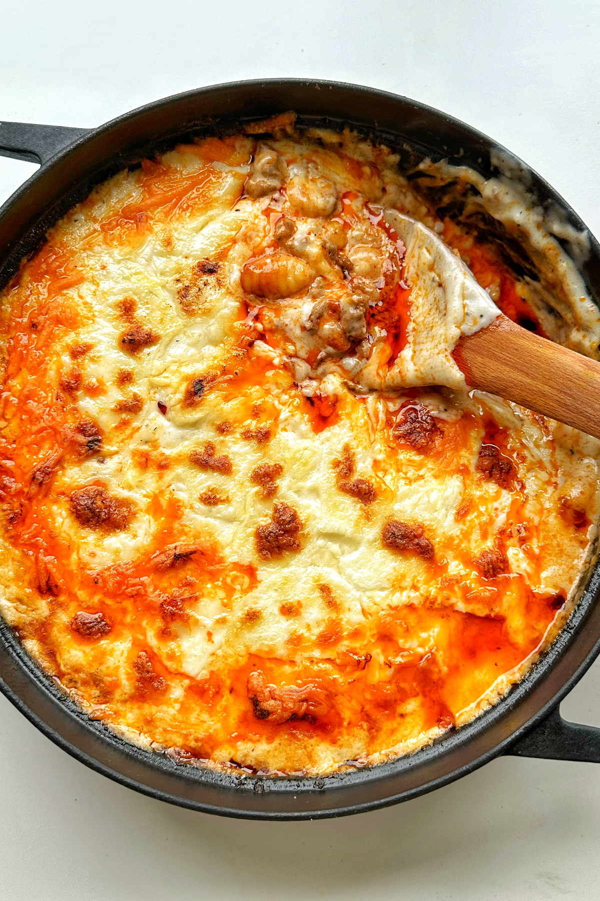 Black casserole dish filled with gochujang gnocchi lasagne with wooden spoon.