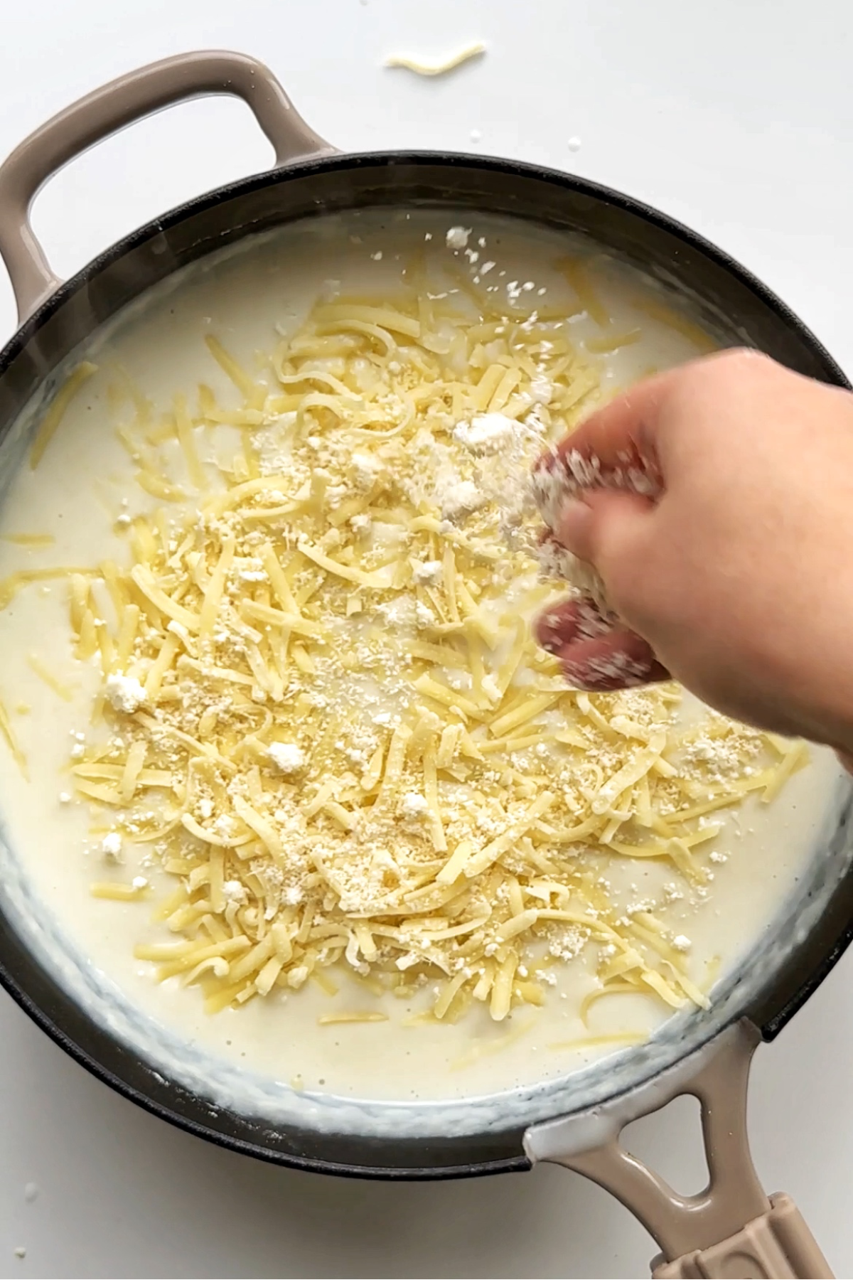 Sprinkling parmesan cheese over a béchamel sauce in black pan.