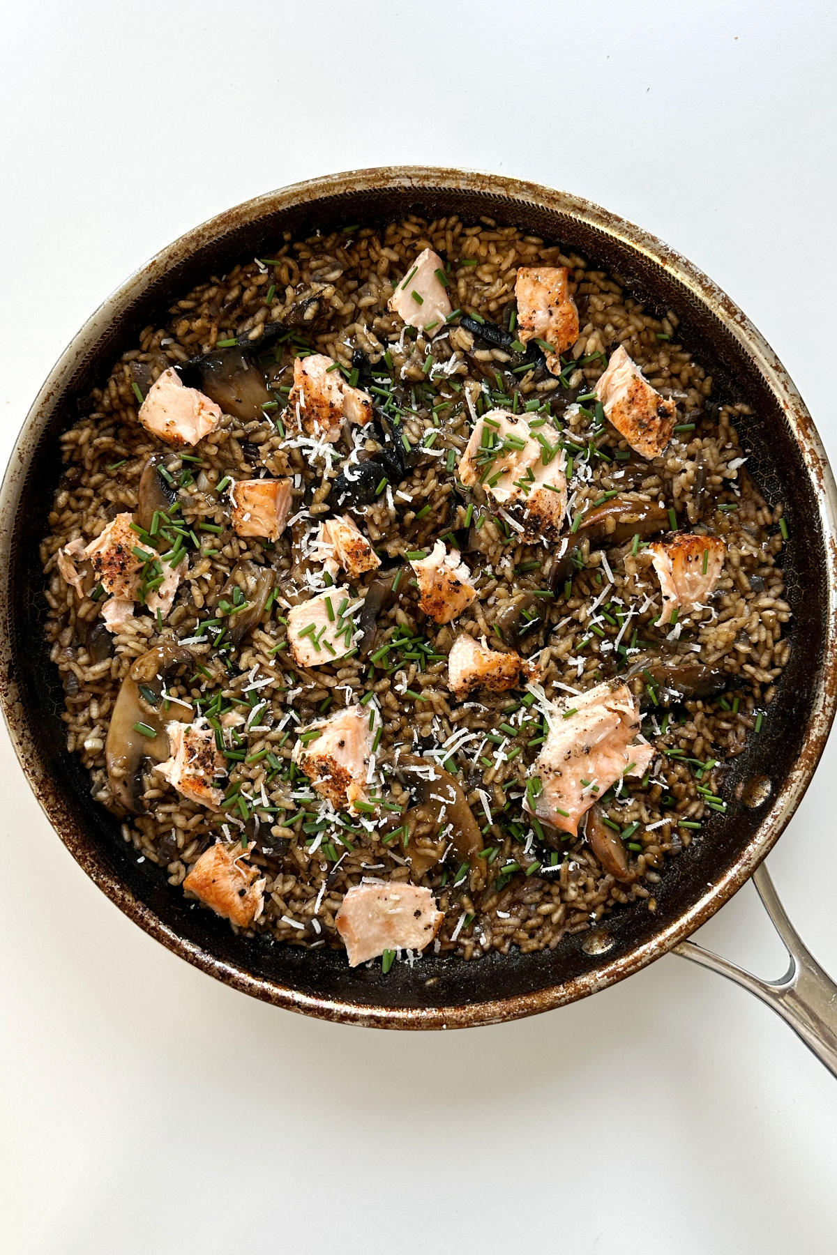 Salmon and mushroom risotto in black pan topped with parmesan cheese and chopped chives. 