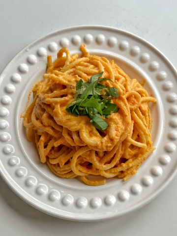 White plate topped with a creamy bucatini pasta, garnished with basil.