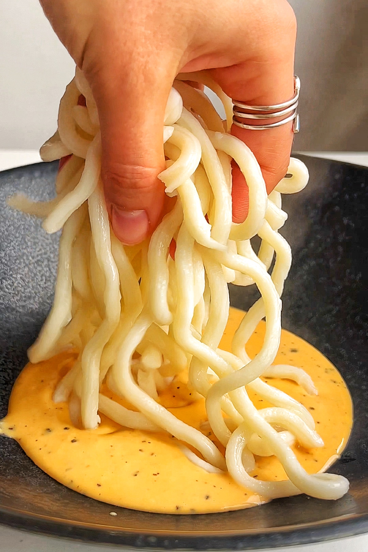 Adding udon noodles into carbonara sauce.