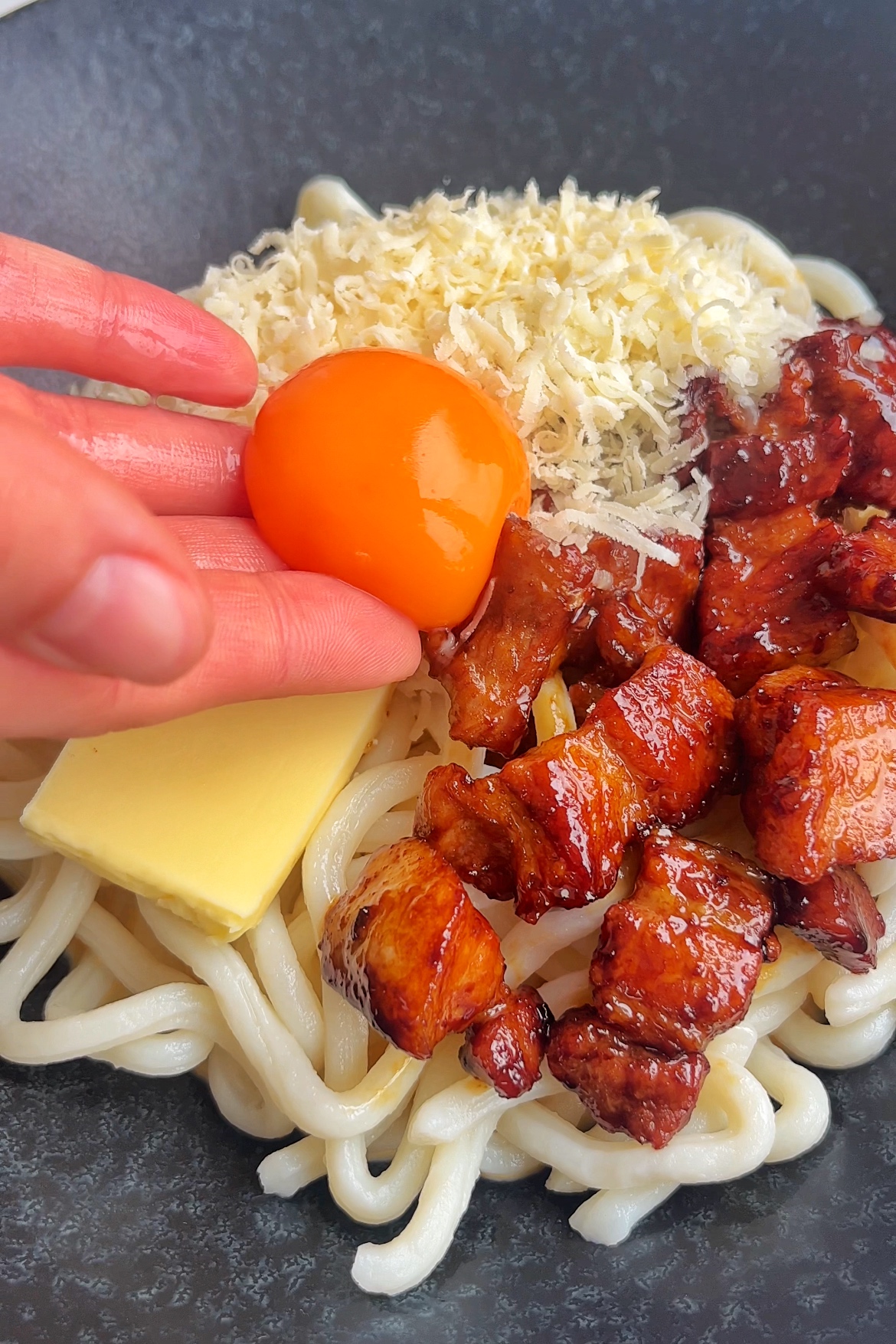 Assembling pork belly udon carbonara placing an egg yolk on top.