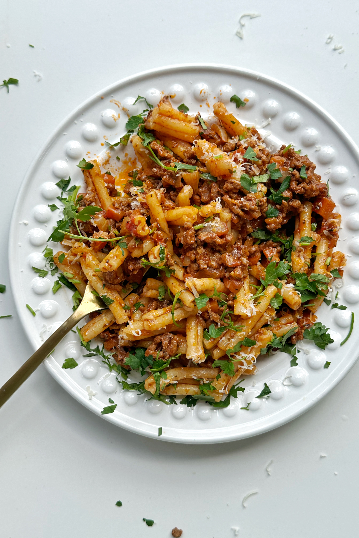 A bowl of casarecce bolognese with a fork in a white bowl. 