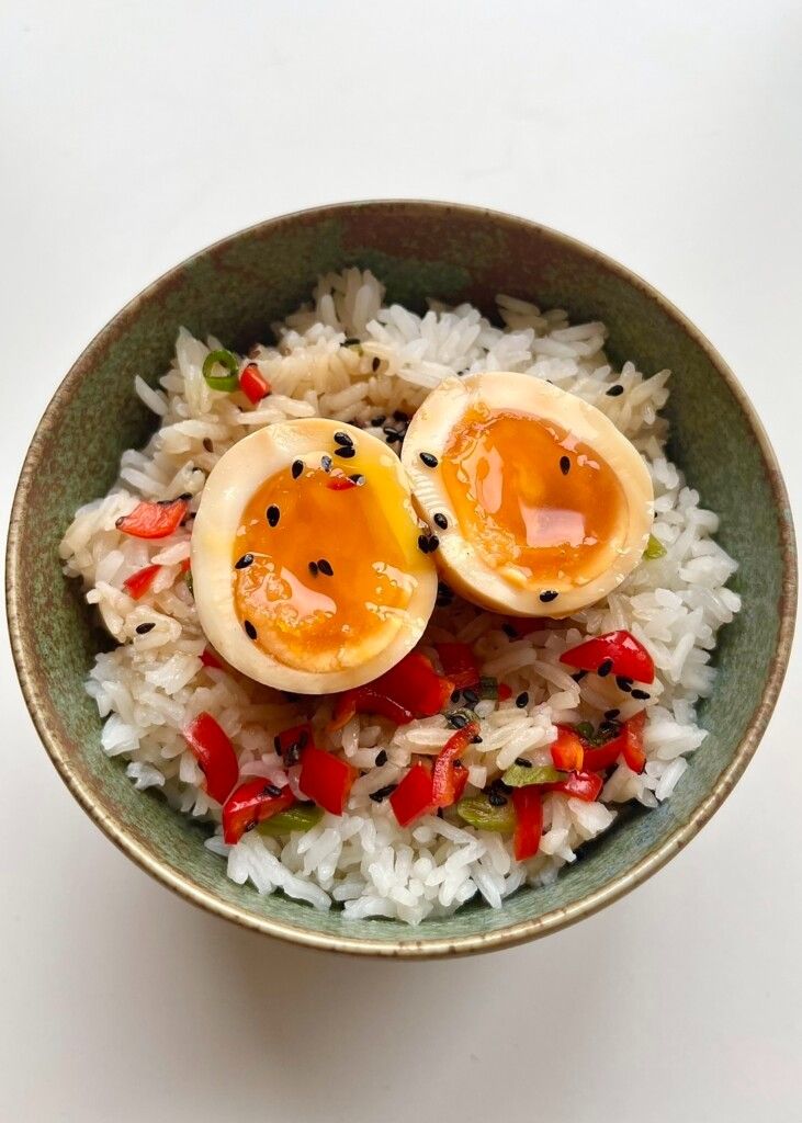 Two perfectly cooked 6.5-minute jammy ramen eggs (Ajitama) with liquid yolks, topped with black sesame seeds and chili, demonstrating the ultimate ramen topping.