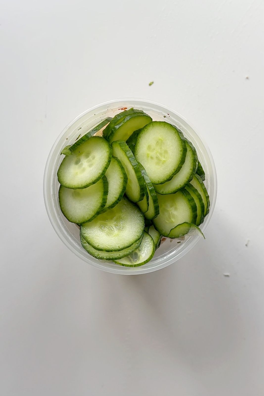 Tupperware with chicken, cucumber, and sweetcorn in it on white background.