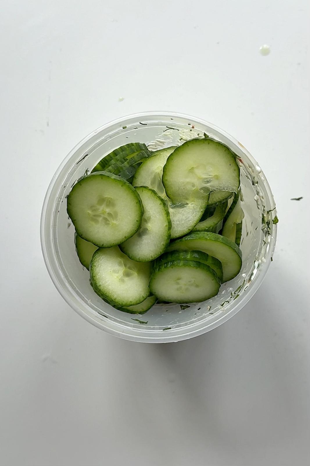 Plastic tupperware filled with cucumber on white surface.
