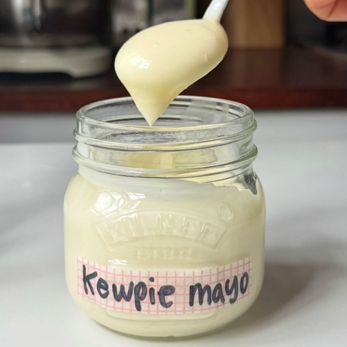 A spoonful of thick, creamy homemade kewpie mayo lifted from a glass jar showing the smooth texture