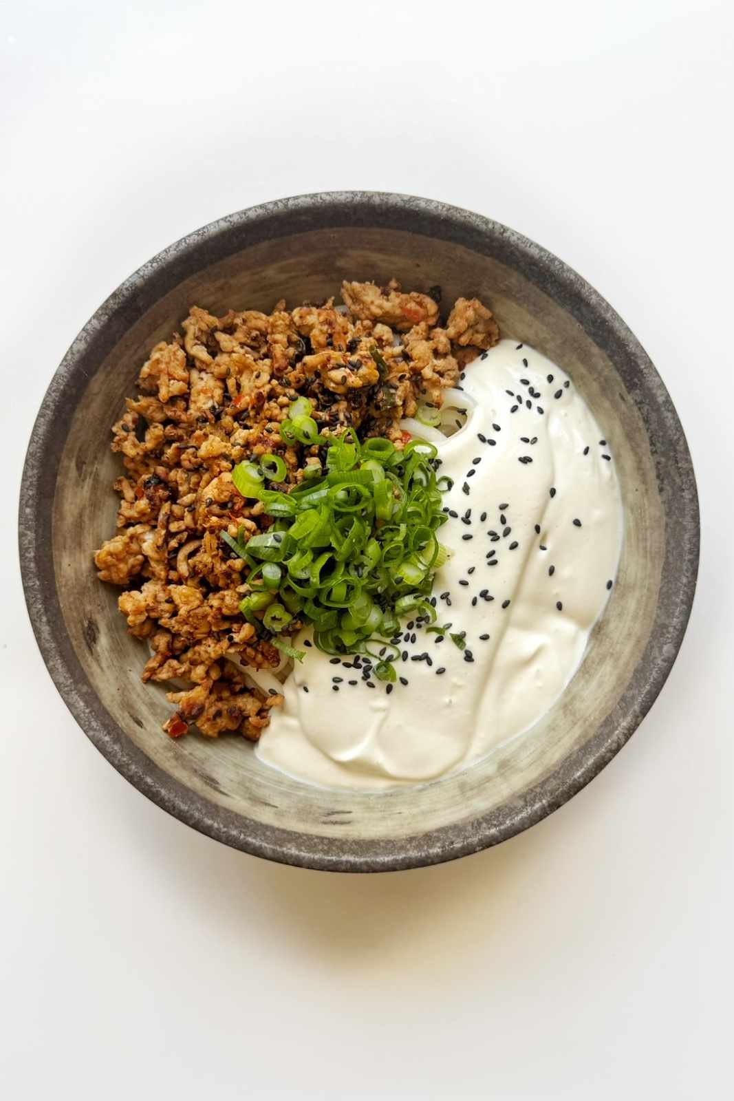 Stone bowl of crispy spiced ground meat next to smooth blended tofu cream, garnished with green onions and black sesame seeds, before mixing