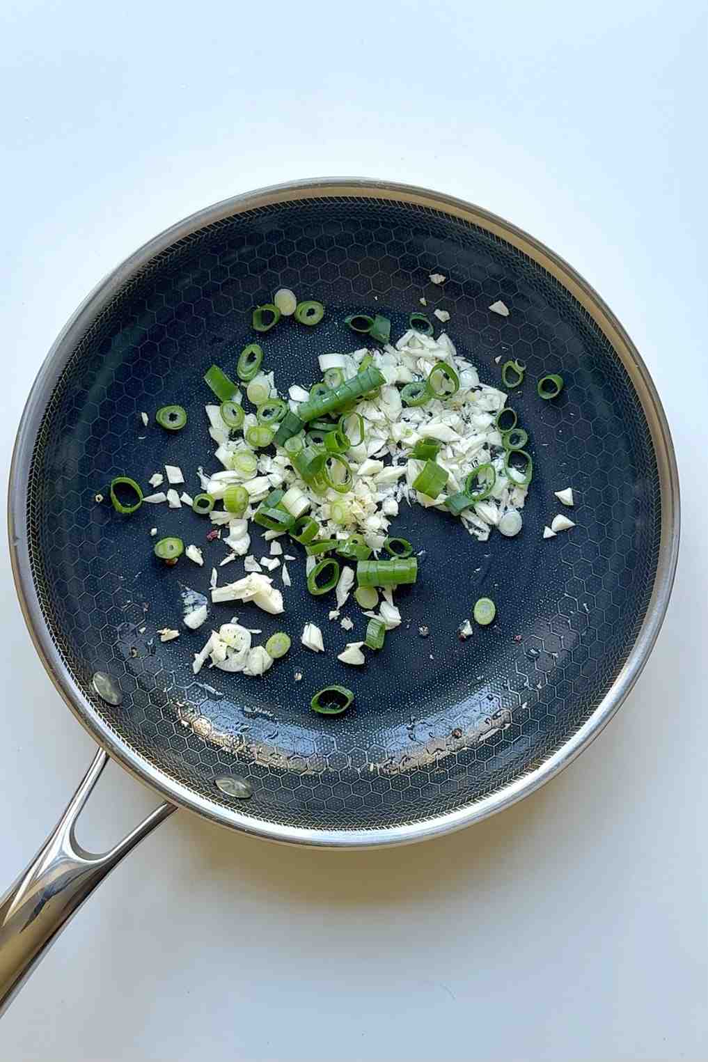 Minced garlic and sliced spring onions sautéing in a stainless steel pan, the first step in making mapo tofu udon