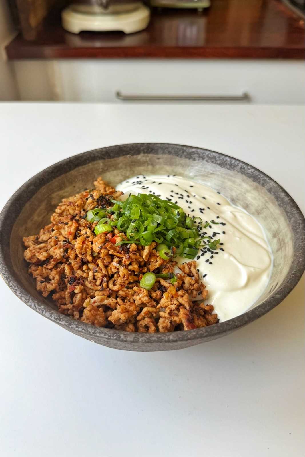Stone bowl of creamy mapo tofu udon with spiced ground pork, blended silken tofu, green onions, and black sesame seeds