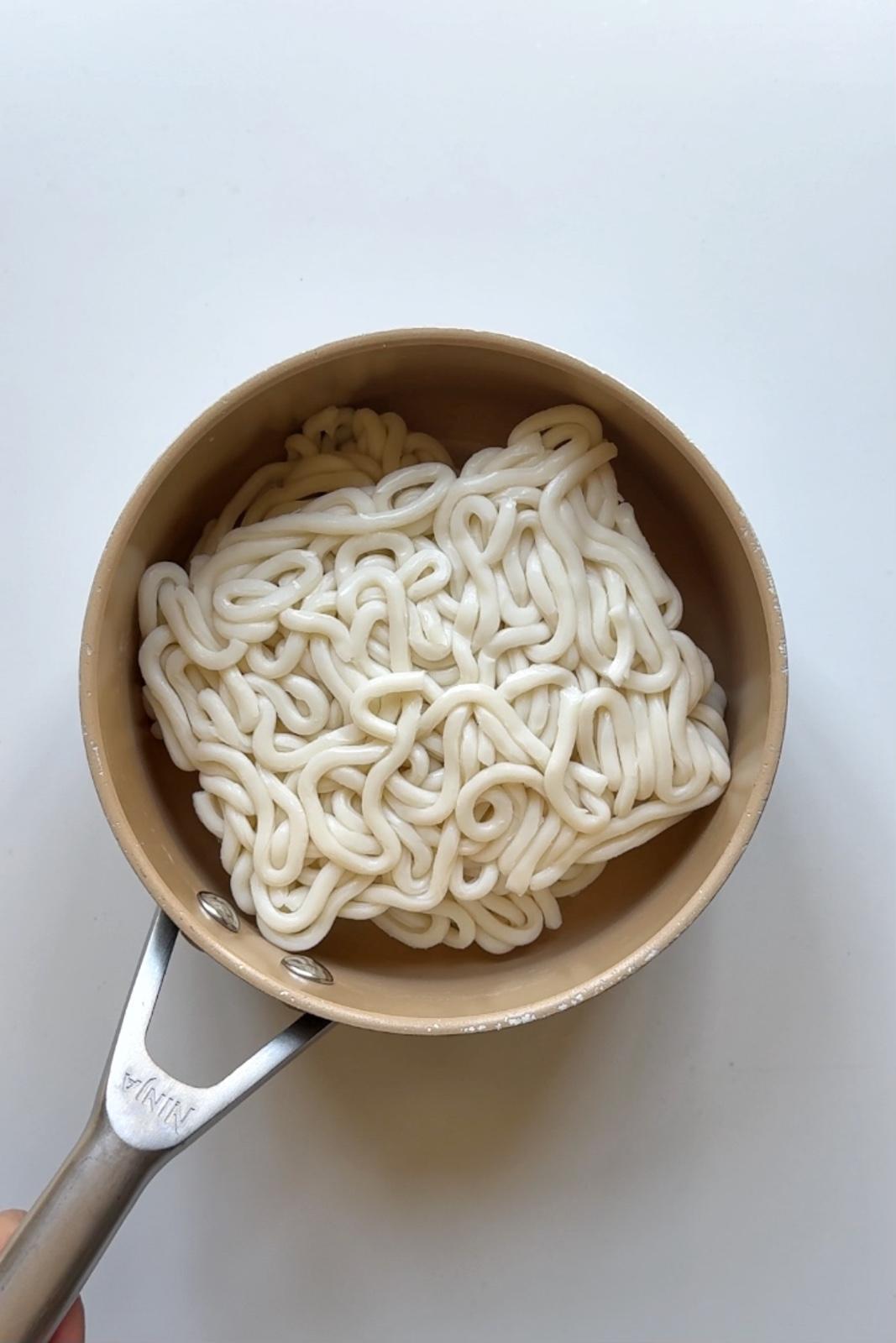 Packaged udon noodles heating in a small saucepan, ready for the creamy mapo tofu sauce