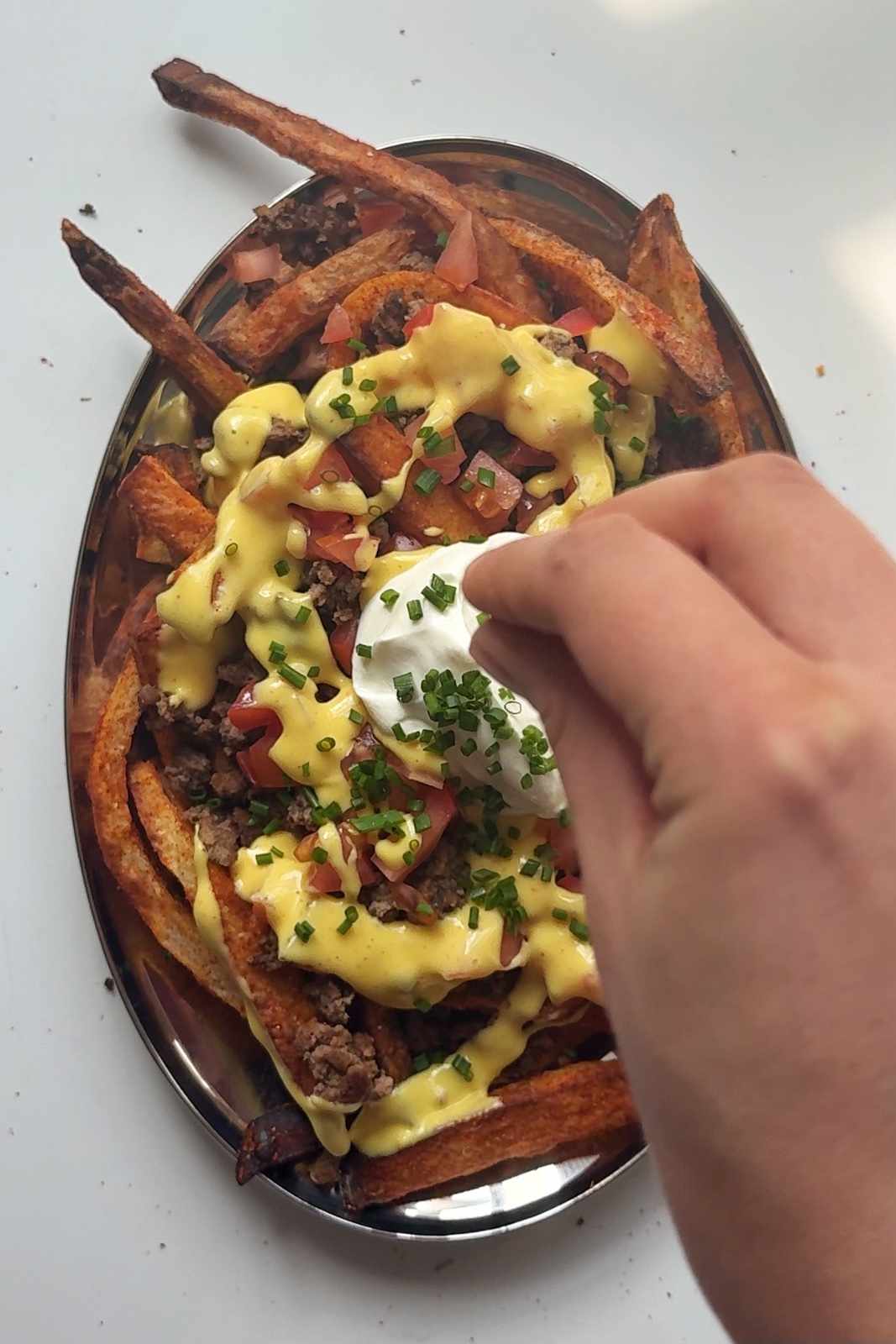 Fully loaded nacho fries with ground beef, nacho cheese sauce, tomatoes, sour cream and chives on a serving platter