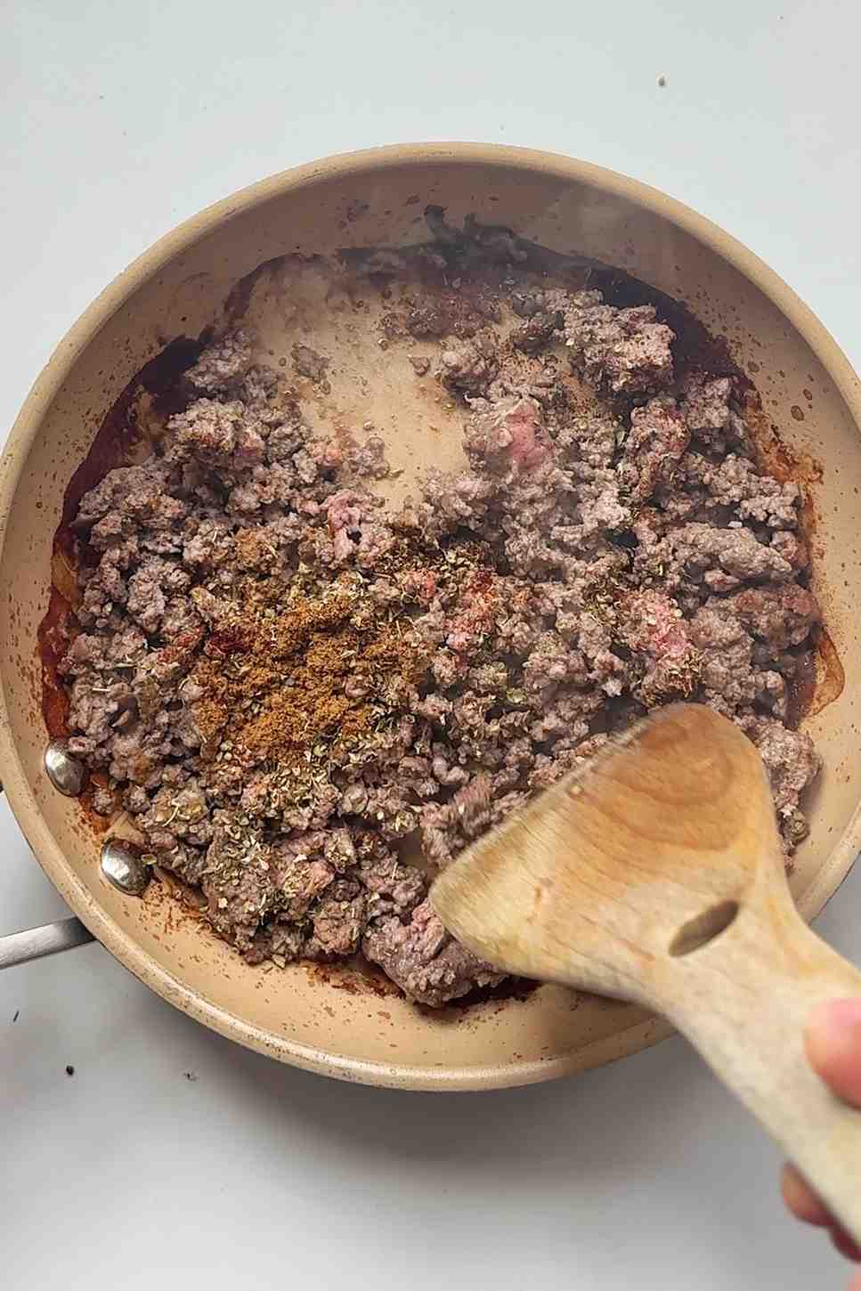 Seasoned ground beef cooking in a skillet with cumin and oregano for nacho fries topping