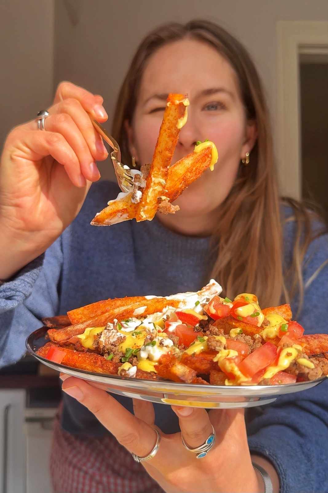 Emily Roz holding a platter of loaded nacho fries and eating one