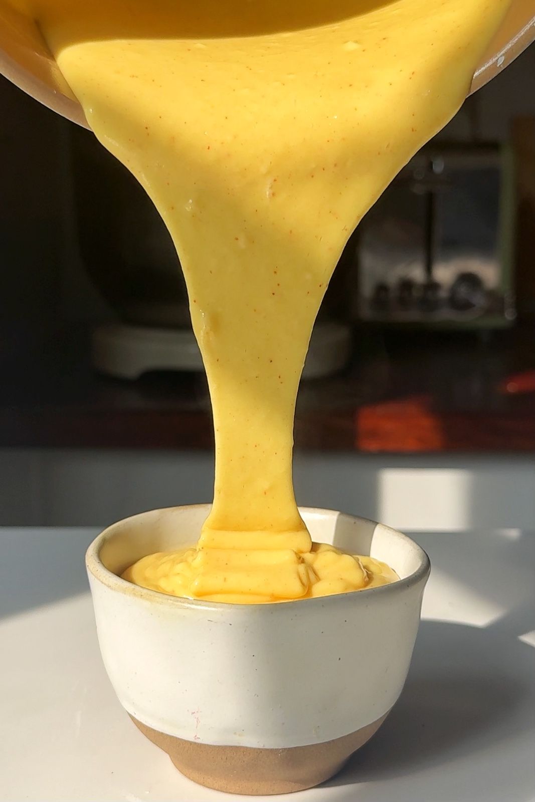 Golden orange nacho cheese sauce being poured into a ceramic bowl