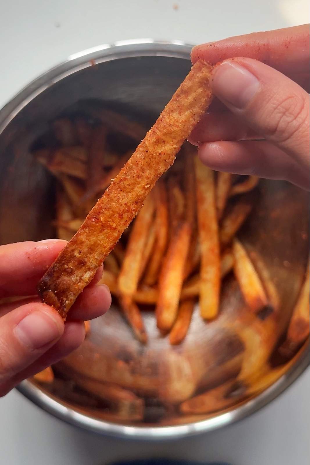 Hand holding a crispy seasoned nacho fry coated in Mexican spices