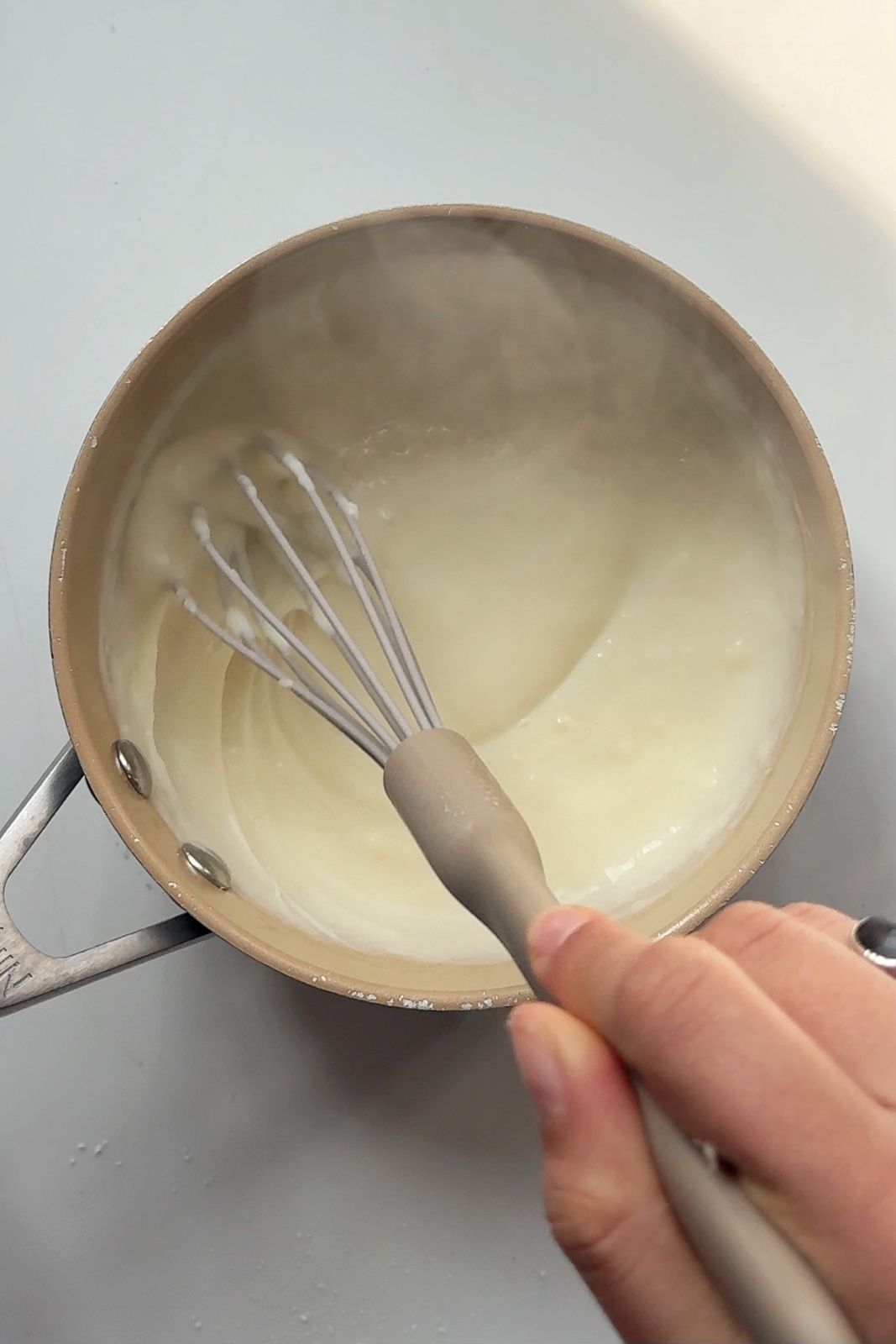Whisking a smooth béchamel cheese sauce in a saucepan for homemade nacho cheese